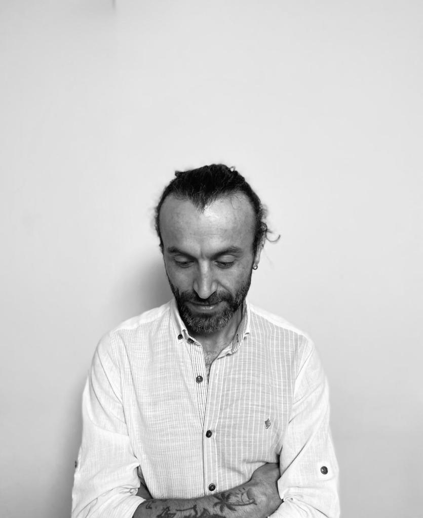 Bir adam, beyaz gömlek giyerek başını eğmiş bir şekilde duruyor.